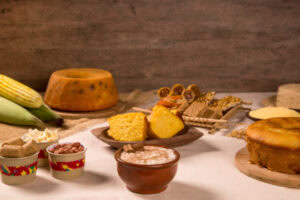 Mesa com doces típicos de Festa Junina, como bolo de milho, bolo de fubá com goiabada, cone recheado, etc.