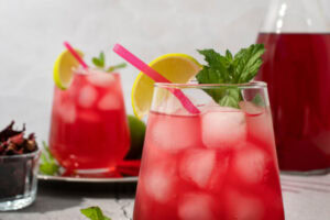 Copo com drinks rosa, pedaço de limão e hortelã na borda.