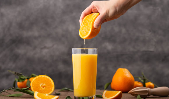 Laranja sendo espremida num copo de suco.