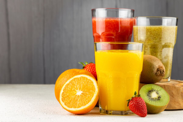 Três copos de suco naturais: morango, laranja e kiwi.