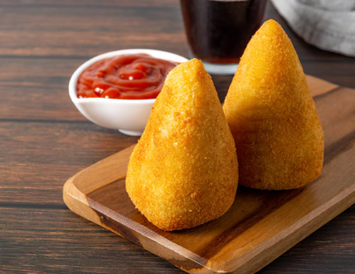 Duas coxinhas sobre tábua de madeira e ao lado de pote branco com ketchup.