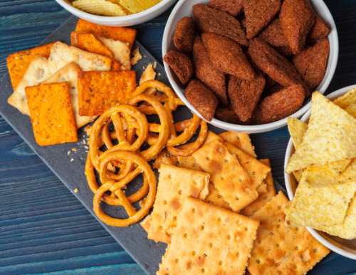 Petiscos em prato e potes, incluindo mini pretzel, biscoitos e batata chips.