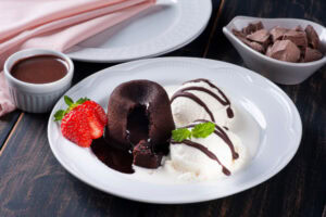Prato com petit gateau, sorvete de creme com calda de chocolate e morango fatiado.