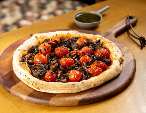 Pizza vegana, com cogumelo e tomate, sobre tábua de madeira.