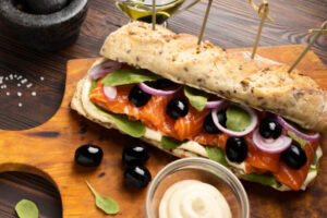Sanduíche gourmet com salmão sobre tábua de madeira.